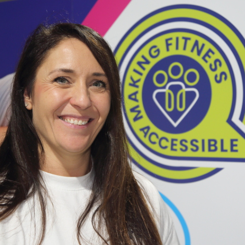 Caroline, Inclusive Exercise Coach at The Angel Centre, smiling in front of Making Fitness Accessible logo